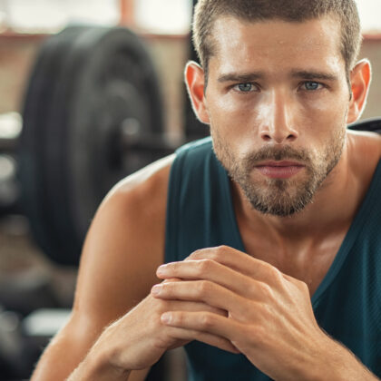 Handsome young muscular man resting in gym while looking at camera. Portrait of competitive and confident sportsman at cross training center. Determined sweaty guy taking a break after working out session with copy space.